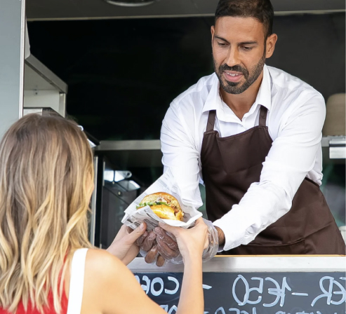 Mitarbeiter eines Foodtruck Caterings bei der Essensübergabe eines Burgers.