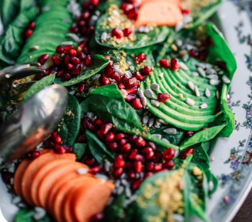 Avocado, Granatapfel und diverses Gemüse angerichtet auf einem Teller. Teil eines veganen Caterings.