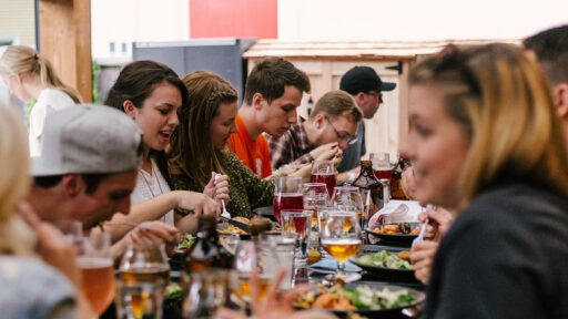 Mehrere Personen an einem langem Tisch am Essen, Event Catering